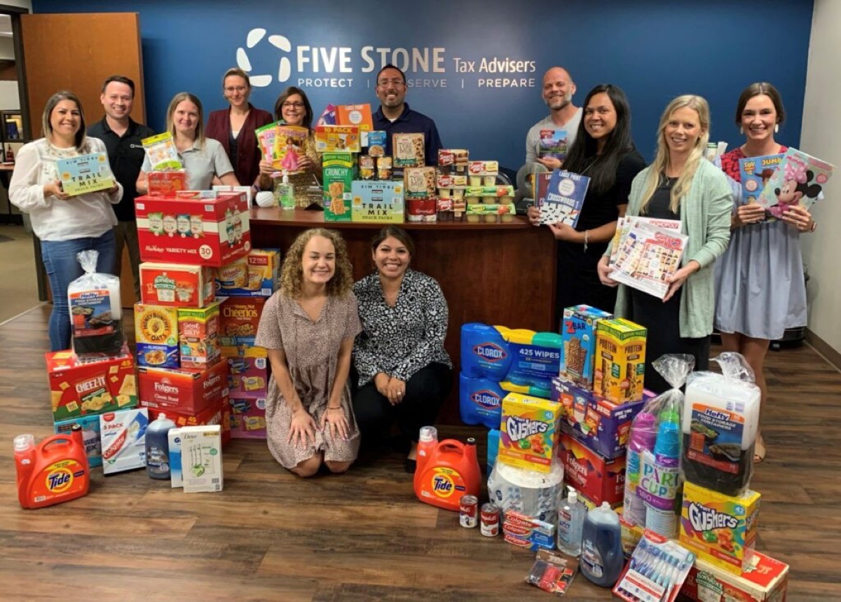 Five Stone team members stand behind a donation drive of groceries, household goods and children's books.