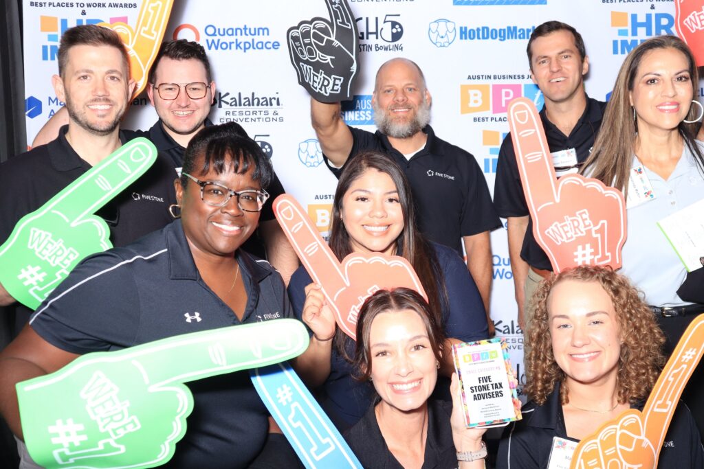 Five Stone team members smile together holding foam fingers at a Best Places to Work awards event.